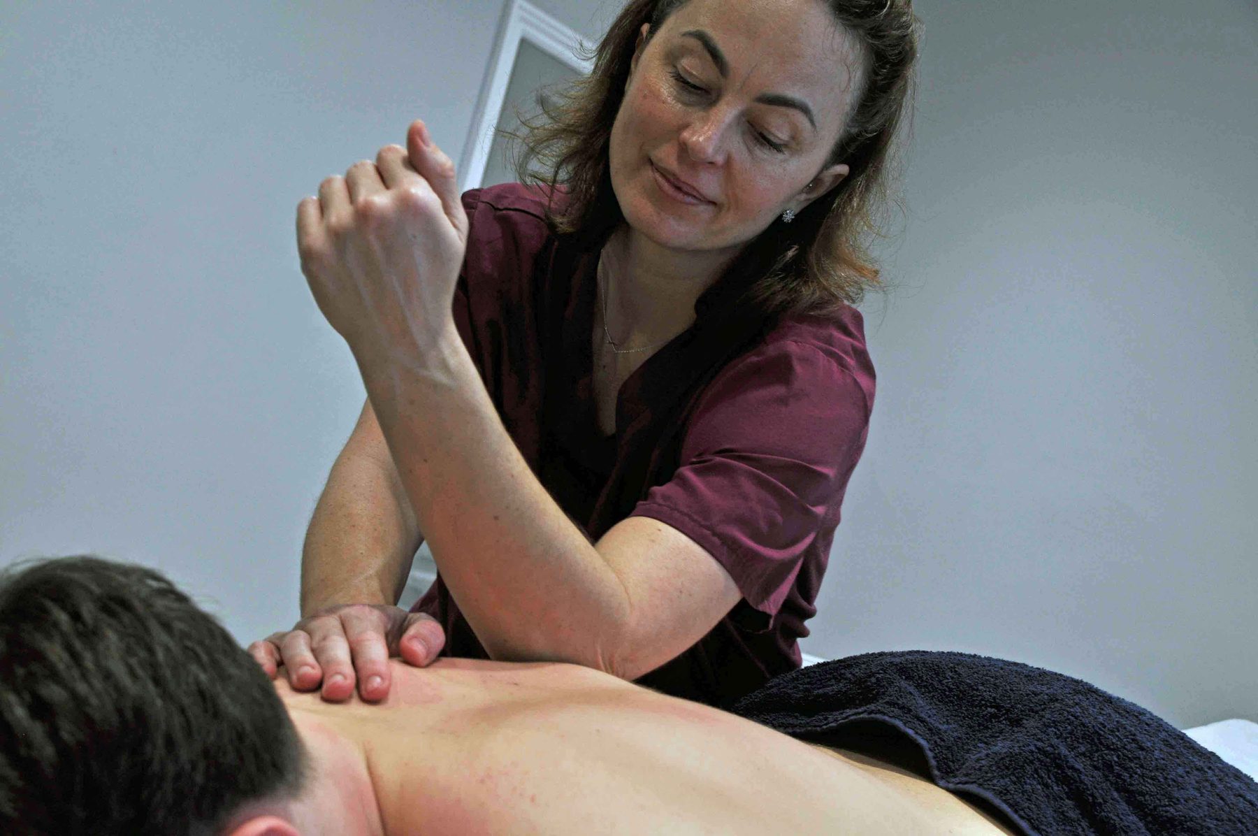 Gosia, in a maroon tunic, working a client's shoulder on the couch