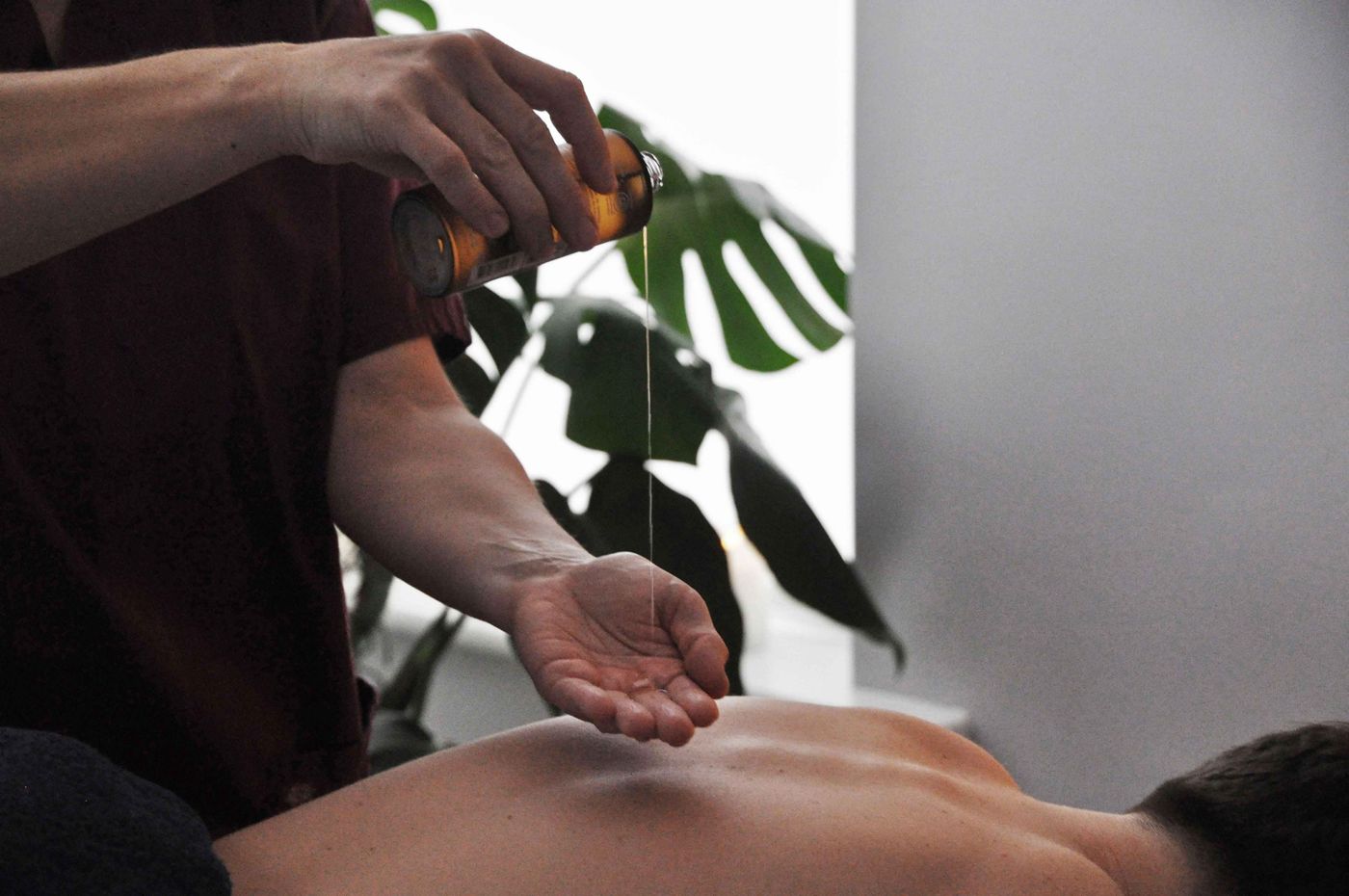Gosia pouring massage oil into her palm, a monstera plant behind