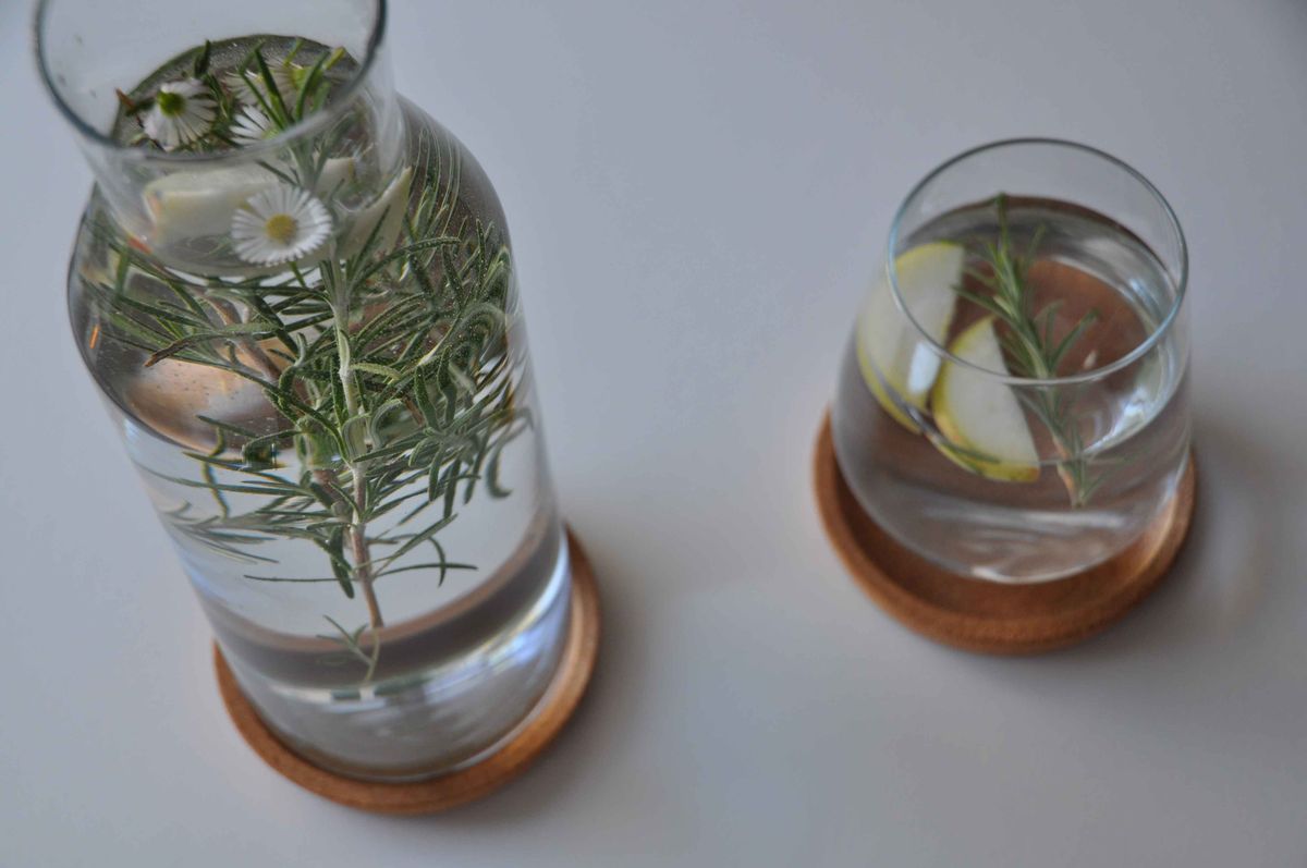 A carafe and glass of water with rosemary and daisies